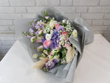Bouquet of flowers wrapped in gray paper on a white surface with a light gray brick wall background