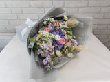 Bouquet of flowers wrapped in gray paper on a white surface with a light gray brick wall background