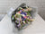 Bouquet of flowers wrapped in gray paper on a white surface with a light gray brick wall background