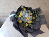 Bouquet of yellow and white flowers wrapped in black paper on a light surface 