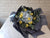 Bouquet of yellow and white flowers wrapped in black paper on a light surface 