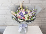 Bouquet of flowers wrapped in gray paper with a white ribbon on a white surface and light gray brick wall background.