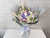 Bouquet of flowers wrapped in gray paper with a white ribbon on a white surface and light gray brick wall background.